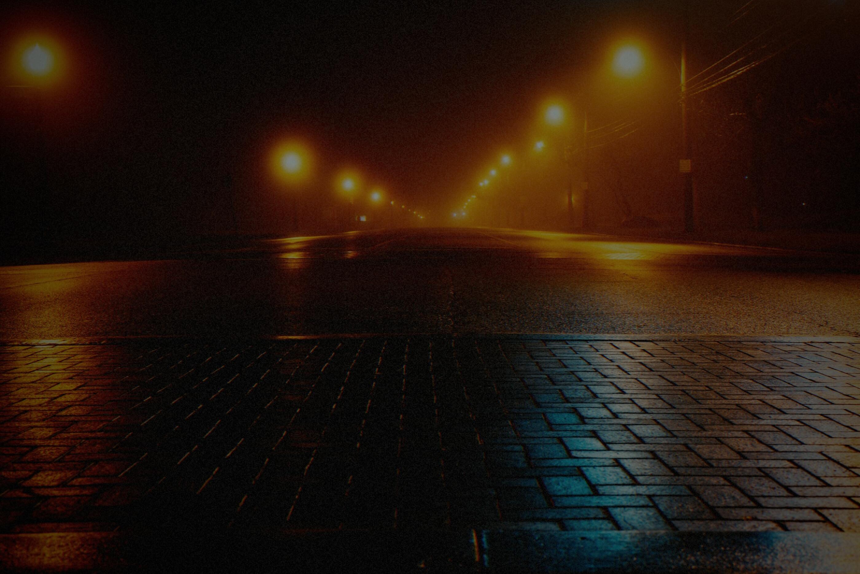 A wet street at night, processed by the Bengala machine: every streetlamp blooms into an amber halo and the shadows drift green-cyan.